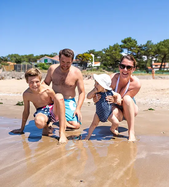 Twee volwassenen en twee kinderen hurken op het strand van La Tranche sur Mer. 
