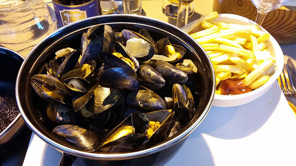 Een pan met mosselen en een bak met friet op een tafel in Frankrijk.