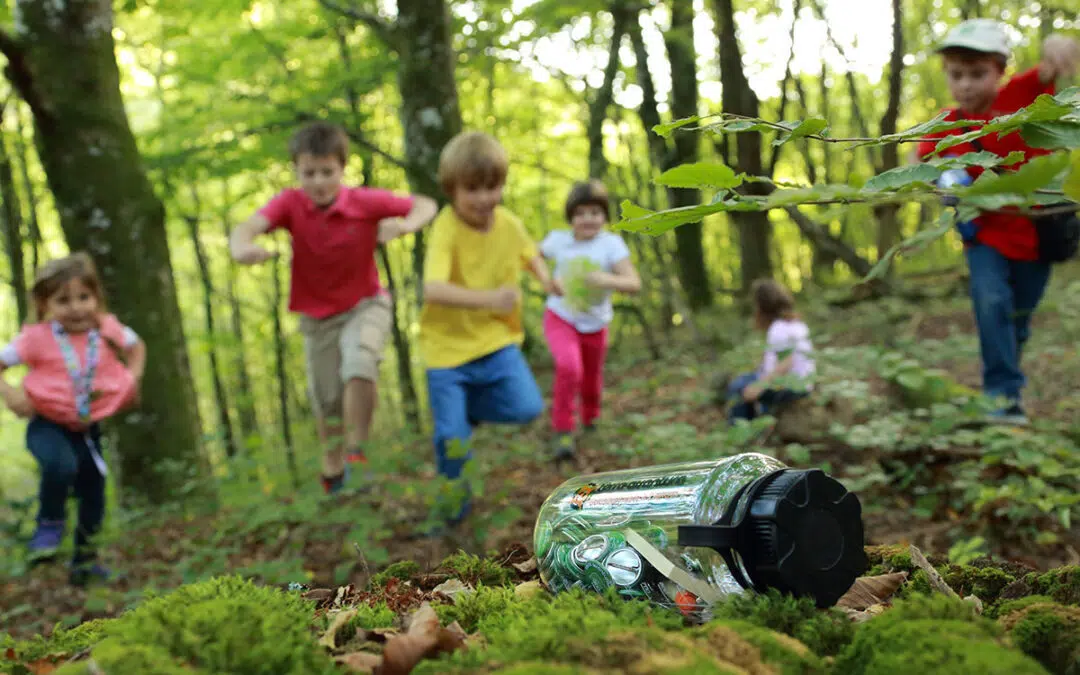 Kinderen rennen naar een fles vol doppen midden in een bos.